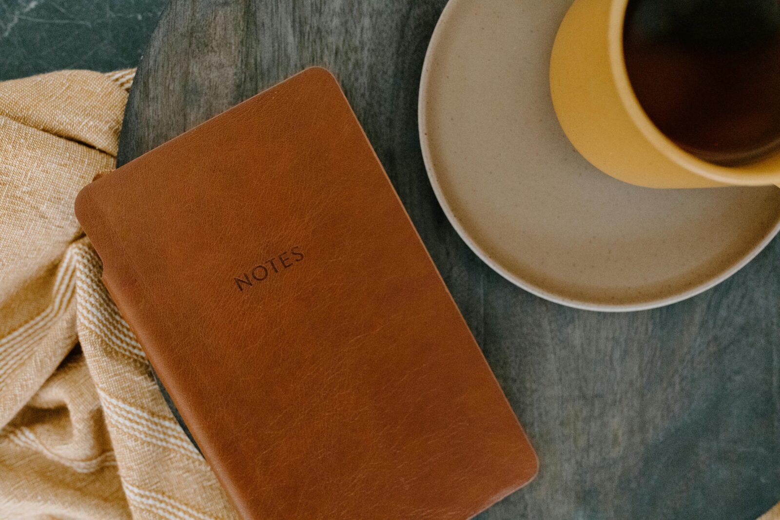 Top view of a leather notebook and coffee cup on a wooden table, perfect for productivity themes.