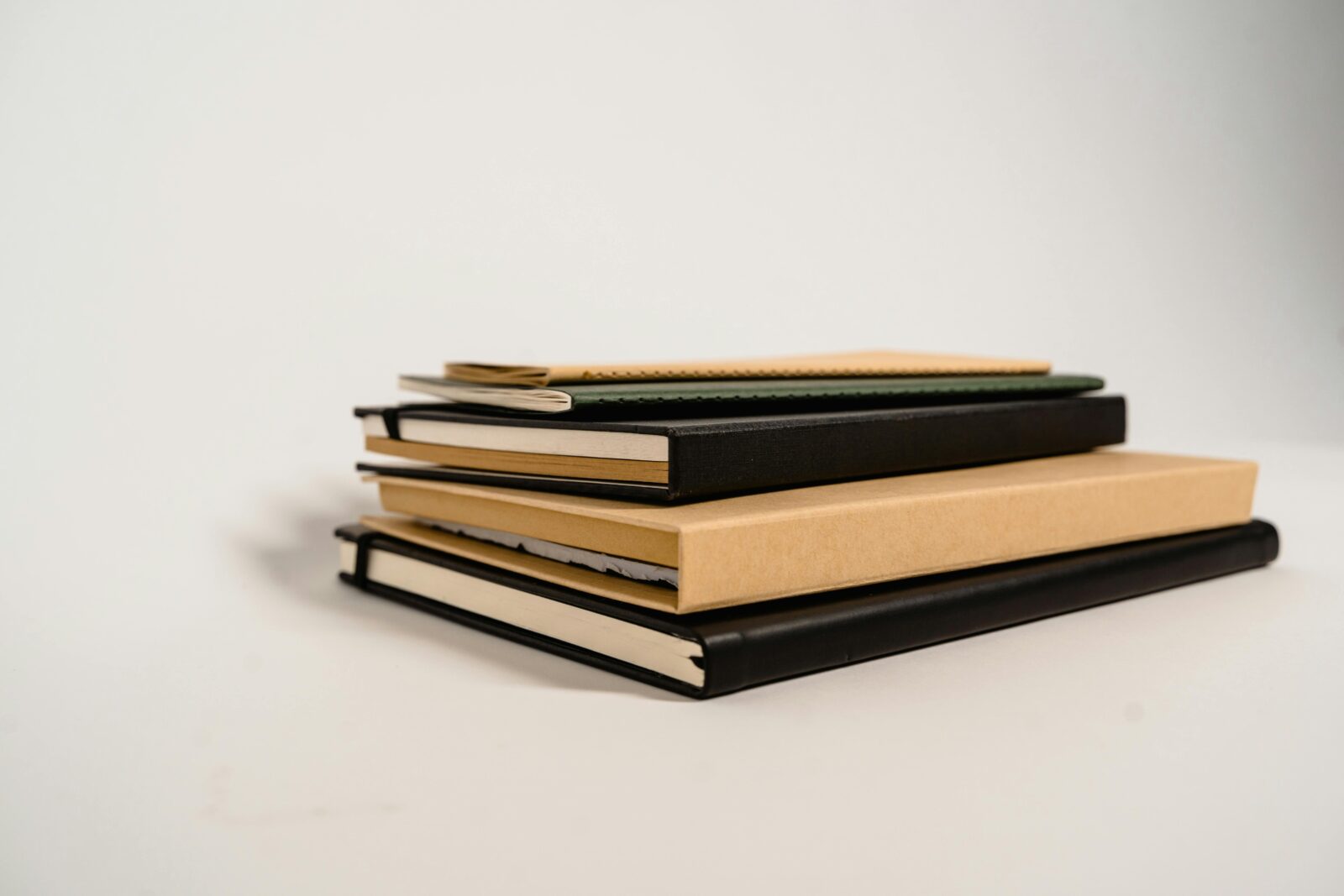 A stack of assorted notebooks with different colors and textures on a white background.